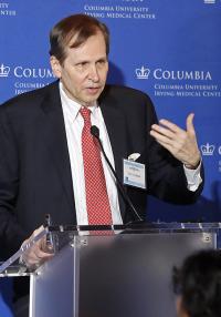 A man wearing a red tie speaks at a podium